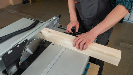 Close-up of a man cutting a wooden board on a circular machine.