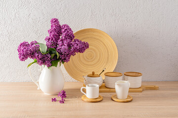A set of white ceramic jars for bulk products and a cup of morning coffee on the kitchen countertop with a bouquet of siren in a white jug.