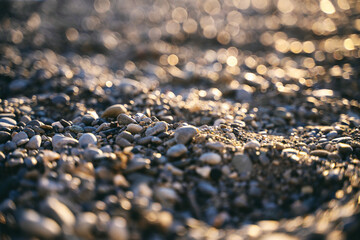 Vet pebbles on the beach shining at sunlight, abstract marine background with bokeh