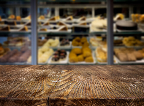 An empty wooden table against the background of a display case with sweets. Cafe, restaurant, coffee shop. Background. The backdrop. Evening. Night. Interior. Confectionery. Sweets. Copy space