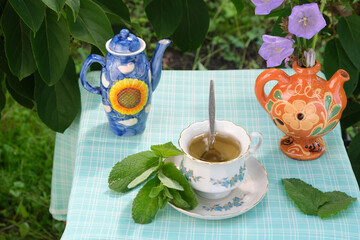 mint tea in nature in a bowl, mint leaves, sugar bowl, flowers in a vase