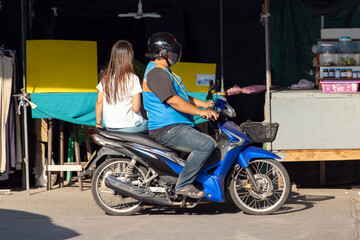 A taxi driver on a motorcycle rides with a woman at a marketplace, Thailand