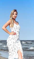 Happy blonde woman in free happiness bliss on ocean beach standing straight. Portrait of a female model in white summer dress enjoying nature during travel holidays vacation outdoors