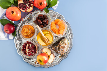 A silver plate with traditional treats for the Jewish New Year. The concept of the holiday of Rosh Hashanah. Top view. Blue background.