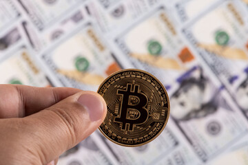 A gold coin with the symbol of the Bitcoin cryptocurrency against the background of 100 US dollar bills