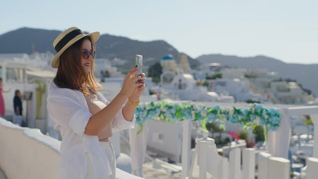 Tourist travel woman in Oia, Santorini, Greece. Happy young woman taking pictures at landmark destination. 
