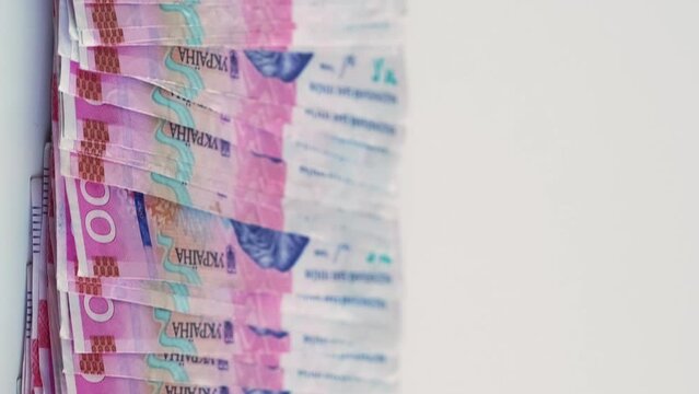 Vertical video. Cash money. Ukrainian hryvnia. UAH currency. 200 hrn bill pink blue color paper banknotes pile on white empty space background.