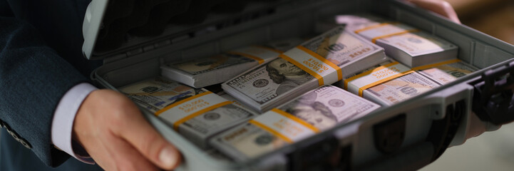 Businessman in suit holding suitcase full of currency money closeup. Profitable financial deals concept