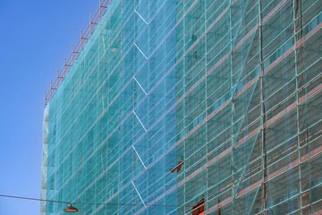 Foto auf Acrylglas Großes eingerüstetes Gebäude in einer Stadt, gesichert mit schützenden Netzen, seitliche Detailansicht, Himmel, Copy Space © redaktion93