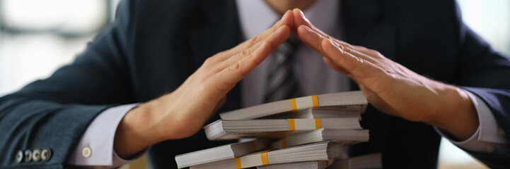 Male banker protecting with hands lot of banknotes closeup. Secure storage of money savings in bank...