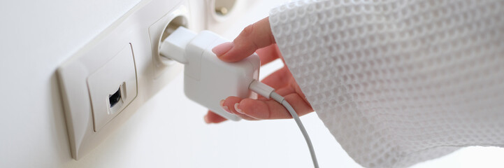 Woman in white bathrobe inserting plug into outlet at home with hand closeup. Energy saving concept