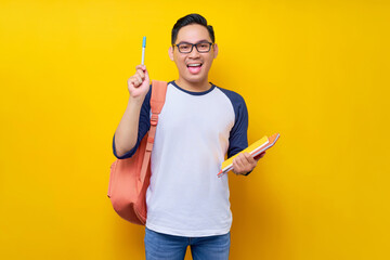 Excited young Asian man student in casual clothes bag holding book and pen, pointing finger up with...