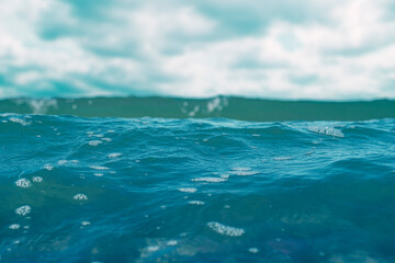Carefree ocean waves. Blue water surface with small waves. Background on the theme of holidays and vacations at sea with the family. Water with white foam in soft focus on a bright sunny day.