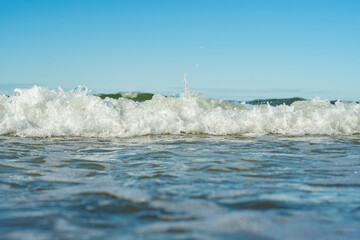 Close-up of the sea wave with the foam surging on the shore. View of sea water in soft focus. Background in a light blur on the theme of a serene summer vacation and relaxed vacation.