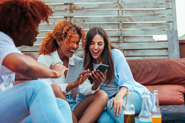 Three young people using phone together while sitting on rooftop