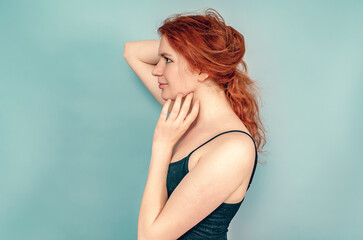 Fototapeta premium Profile of a girl with brown eyes. Hand touches chin. Long red hair, black dress. Gray background.