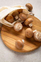 Overhead view of raw mushroom in cotton shopping bag and kitchen board