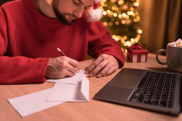 Bearded man in Santa hat writing greeting cards at home office during christmas