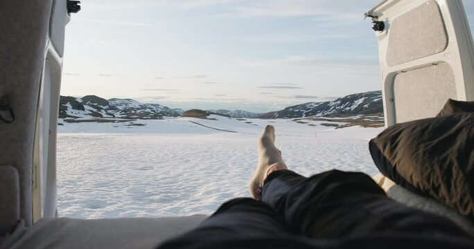 Point of view of crossed feet inside campervan in snowy Aurland mountain sunset