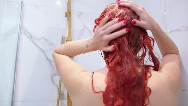 Woman washing long red color hair in modern shower, back view