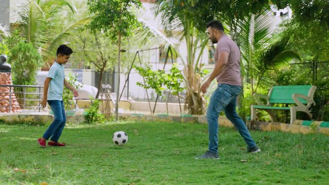 Happy indian father with little son playing football game at park - concept of weekend holidays, Family recreation and active bonding.
