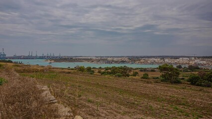 Green farming Town of Marsaxlokk in Malta in the distance alongside a harbour. Timelapse panoramic shot.