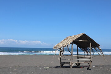 beach hut with blue sky, grey sand, and rubbish around it