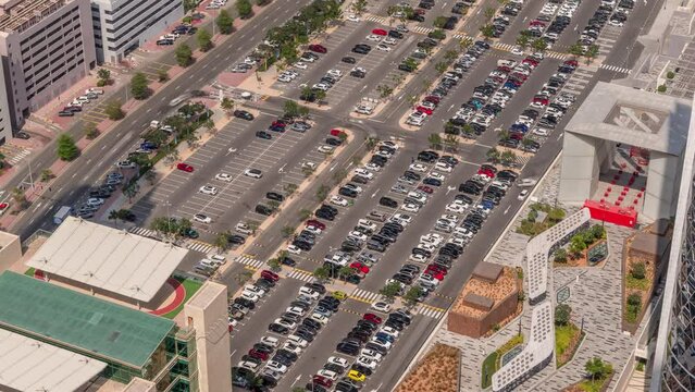 Aerial view of many colorful cars parked on parking lot with lines and markings for parking places and directions timelapse during all day. Long shadows moving fast. Dubai financial center