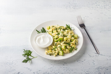 Turkish scrambled eggs with zucchini served with yogurt on a light blue background. Delicious homemade vegetarian food