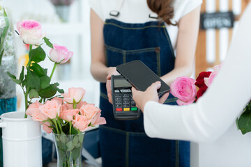 Cropped shot of female florist holding smartphone paying for flowers in flower shop