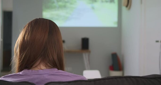 Woman looks at projection of an image on wall. Work home projector, rear view. Home theater concept