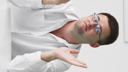 Vertical video. Applauding man. False congrats. Sarcastic emotion. Skeptic guy clapping hands expressing silly joy sitting desk in light room interior.