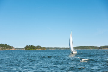 Obraz premium Sailboat with wind in its sails on the blue ocean water in a picturesque archipelago with green islands on a clear summer day for a success and recreational sailing concept
