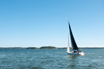 Sailboat with black sail as seen from the aft sailing on turquoise water on clear blue sky day in Stockholm archipelago in Sweden
