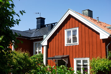 Gable of a traditional vintage falu red house with white corners and trims in rural Swedish Stockholm archipelago with lush green garden in summer with clear blue sky with no clouds - obrazy, fototapety, plakaty