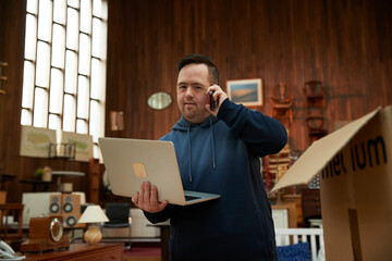 Worker with Down syndrome talking on phone and using laptop in furniture shop