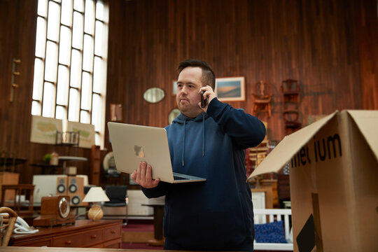 Worker with Down syndrome talking on phone and using laptop in furniture shop
