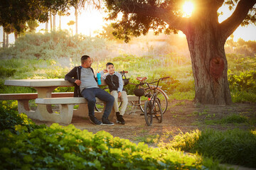 Father and son (12-13) relaxing in park after bike ride