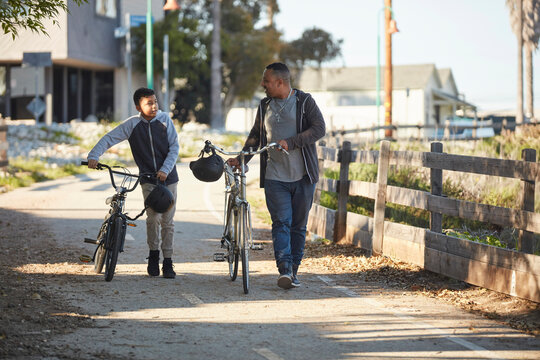 Father and son (12-13) walking with bicycles