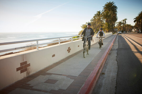 Father and son (12-13) riding bicycles on coastal road