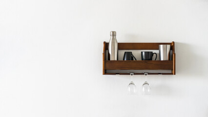 A shelf with mugs and glasses in the kitchen on a blank white wall. Storage of kitchen utensils and glasses. Stylish modern kitchen design concept. Copy space panoramic header
