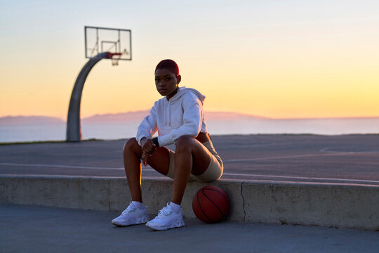 Portrait of mid adult woman sitting on basketball at sunset