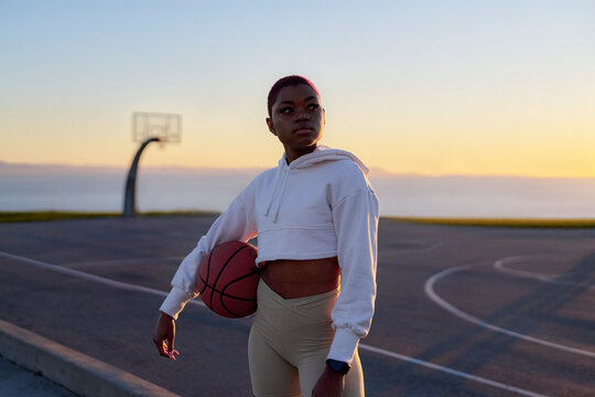 Mid adult woman holding basketball at sunset