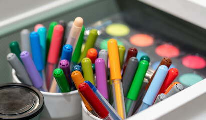 Bunch of colorful pencils markers in cups in drawer. Art school accessories. Paint set.