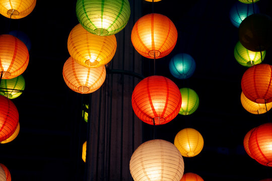 Many round Chinese paper lanterns hanging in the dark. A lot of festive colorful decorations prepared for a celebration in an oriental style