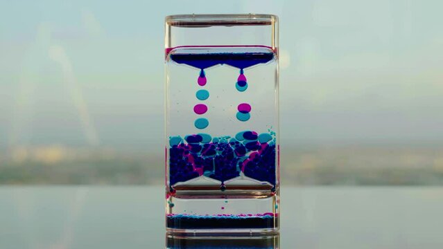 Liquid oil hourglass : Double color liquid oil falling down through a narrow neck in a timer hourglass in city background, Indicating passing of time, Abstract background with moving