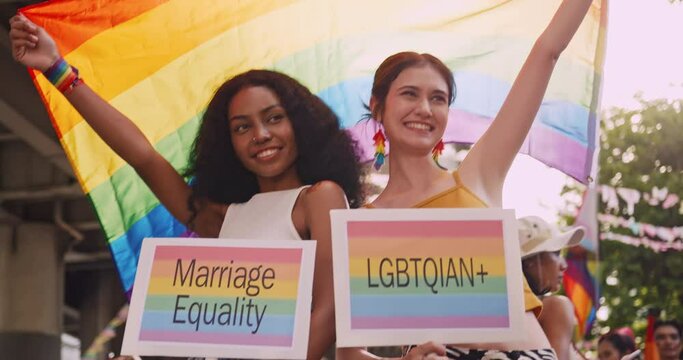 A lesbian couple with a rainbow tattoo sticker and flag representing the symbol of homosexuality in a pride parade.