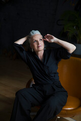 Fototapeta na wymiar lifestyle portrait senior woman with gray hairrelaxes in a black shirt and trousers rests in a chair. copy space. greyhairdontcare. 