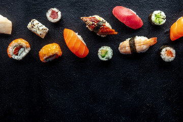 Fototapeta Sushi, shot from the top. Rolls, maki, nigiri on a black slate background, Japanese food. Salmon, eel, shrimp, tuna etc with rice, with a place for text obraz
