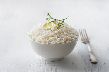 A bowl of steamed long grain rice with butter and a sprig of dill on a light gray background